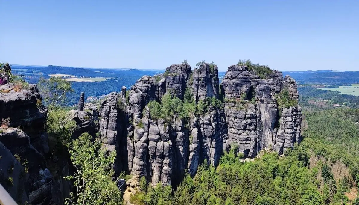 Hohe, senkrechte Felswände ragen aus dichtem Wald; blauer Himmel und Hügel im Hintergrund. | © DAV Markt Schwaben/Josephine Freikamp