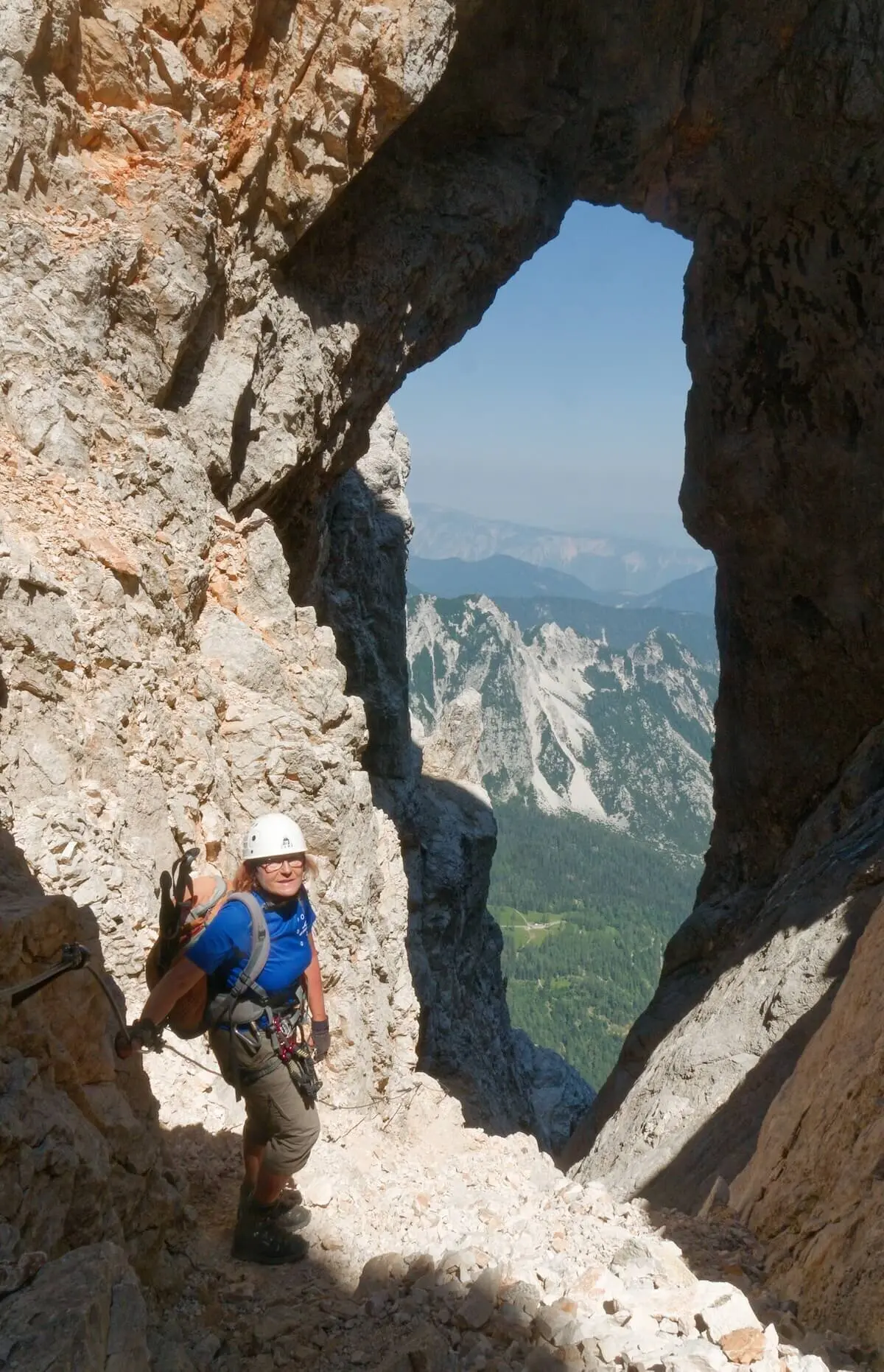 Person steht unter natürlichem Felsbogen mit Blick ins Tal; Kletterausrüstung und Bergkulisse im Hintergrund. | © DAV Markt Schwaben/Lutz Gründel