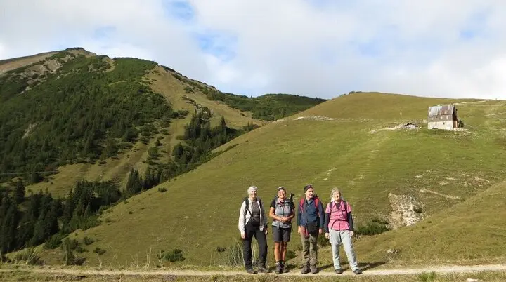 Vier Personen stehen auf Bergpfad vor Wiesen und Wald; Holzhütte rechts, Himmel leicht bewölkt. | © DAV Markt Schwaben/Gerlinde Hübl