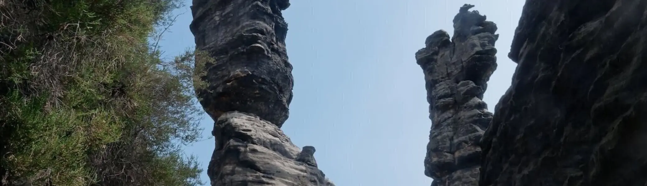 Zwei hohe, schmale Felsformationen ragen senkrecht auf; Person am Fuß der Säulen, Wald und Himmel im Hintergrund. | © DAV Markt Schwaben | Foto Lutz GründelFelsnadeln im Bielatal