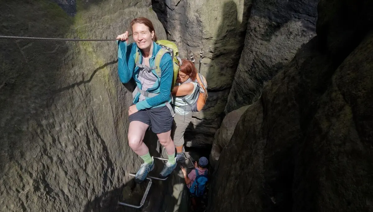 Wandernde steigen durch enge Felsspalte mit Drahtseil und Trittbügeln; mehrere Personen folgen im Hintergrund. | © DAV Markt Schwaben | Foto Lutz Gründel