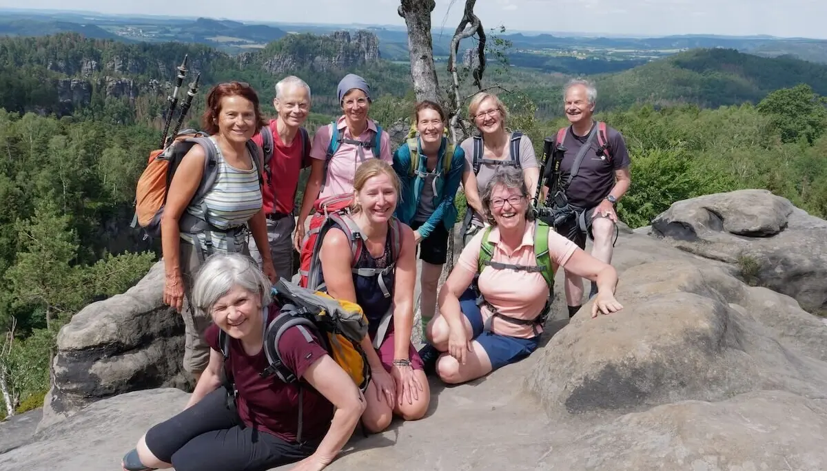 Zehn Personen posieren auf Felsplateau mit Blick auf bewaldete Hügel und Felsformationen unter leicht bewölktem Himmel. | © DAV Markt Schwaben | Foto Lutz Gründel
