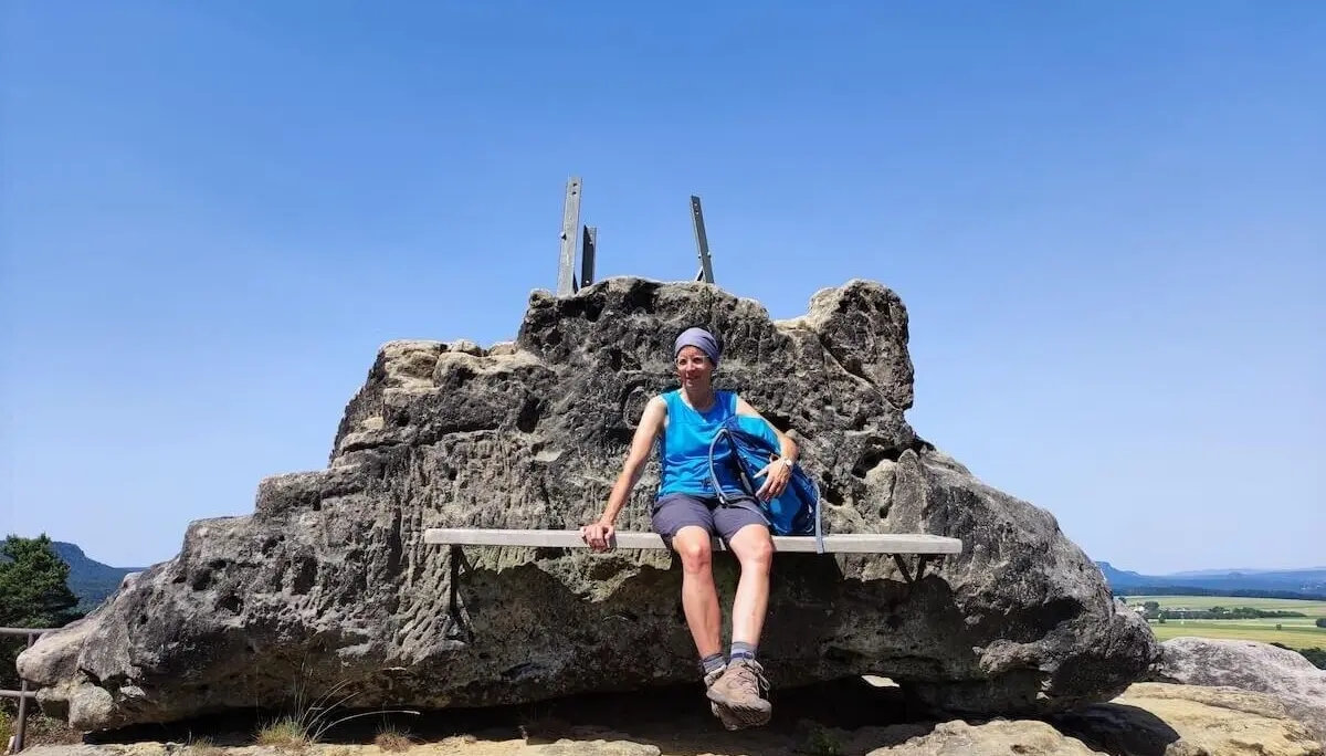 Person sitzt auf Bank im Fels und blickt ins Tal; Rucksack daneben, Felsspitzen und Felder im Hintergrund. | © DAV Markt Schwaben | Foto Josephine Freikamp
