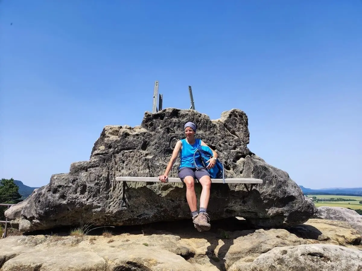 Person sitzt auf Bank im Fels und blickt ins Tal; Rucksack daneben, Felsspitzen und Felder im Hintergrund. | © DAV Markt Schwaben | Foto Josephine Freikamp