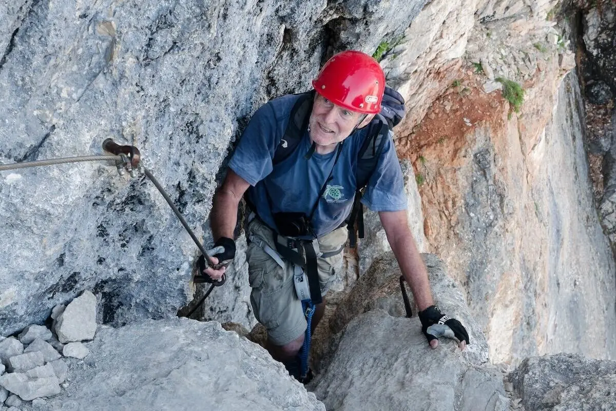 Kletterer mit rotem Helm und Handschuhen steigt durch steile Felsrinne; graue und rötliche Gesteinsstruktur. | © DAV Markt Schwaben | Foto Lutz Gründel