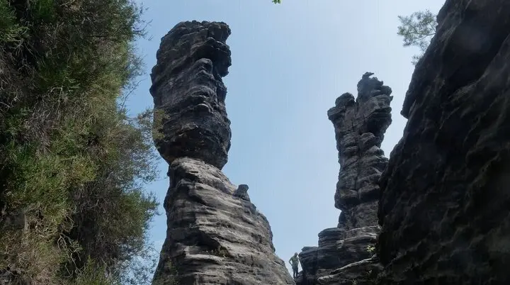 Zwei hohe, schmale Felsformationen ragen senkrecht auf; Person am Fuß der Säulen, Wald und Himmel im Hintergrund. | © DAV Markt Schwaben | Foto Lutz GründelFelsnadeln im Bielatal