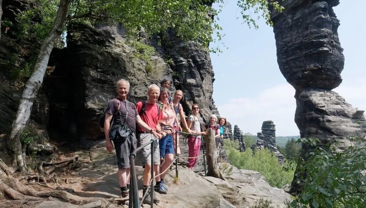 Wandergruppe steht auf Felsweg mit Geländer; markante Felsformationen und Bäume im Hintergrund. | © DAV Markt Schwaben | Foto Lutz Gründel
