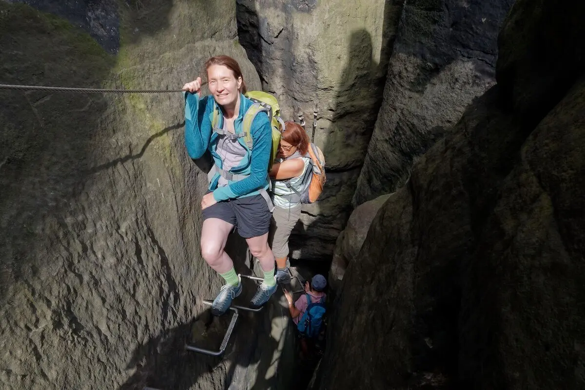 Wandernde steigen durch enge Felsspalte mit Drahtseil und Trittbügeln; mehrere Personen folgen im Hintergrund. | © DAV Markt Schwaben | Foto Lutz Gründel