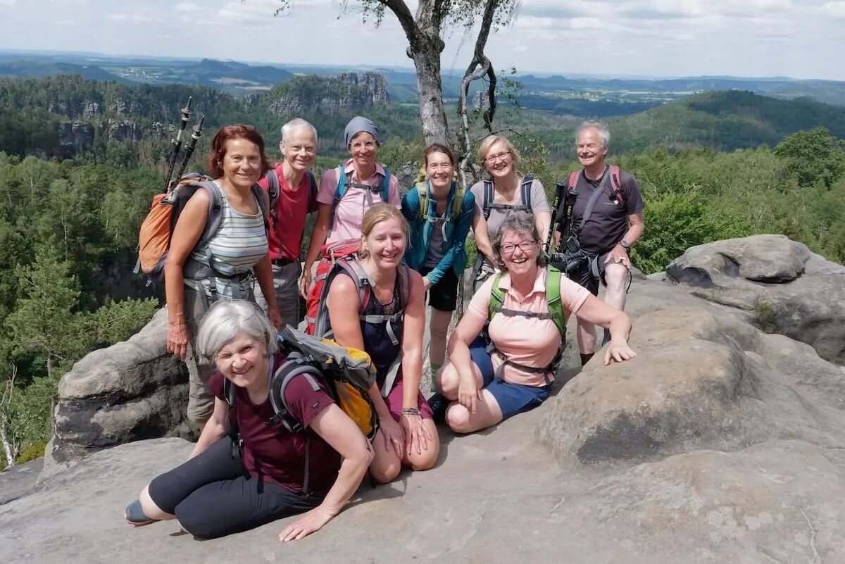 Zehn Personen posieren auf Felsplateau mit Blick auf bewaldete Hügel und Felsformationen unter leicht bewölktem Himmel. | © DAV Markt Schwaben | Foto Lutz Gründel