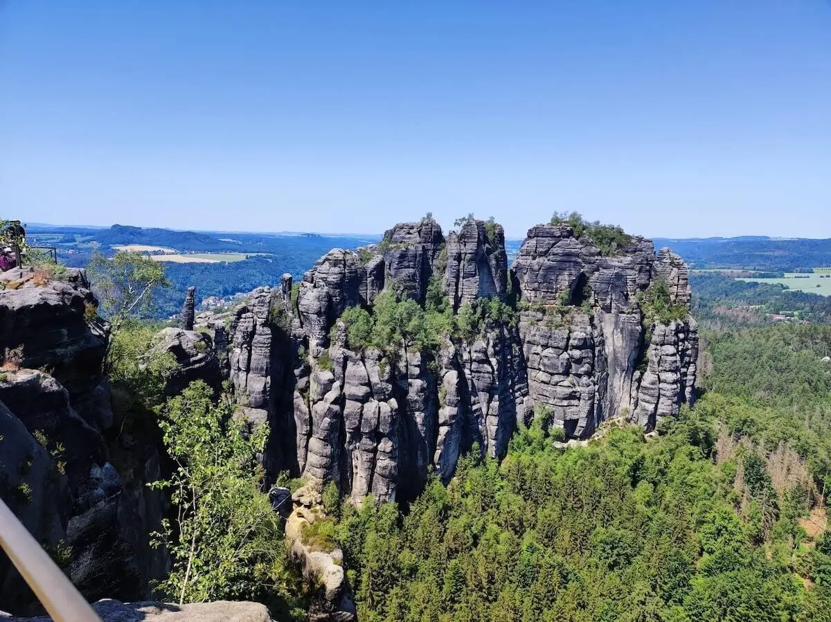 Hohe, senkrechte Felswände ragen aus dichtem Wald; blauer Himmel und Hügel im Hintergrund. | © DAV Markt Schwaben | Foto Josephine Freikamp