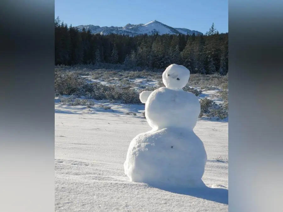 Ein Schneemann steht auf einer verschneiten Almfläche; dahinter verlaufen Waldsaum und schneebedeckte Berggipfel. | © DAV Markt Schwaben / Erwin Matzinger