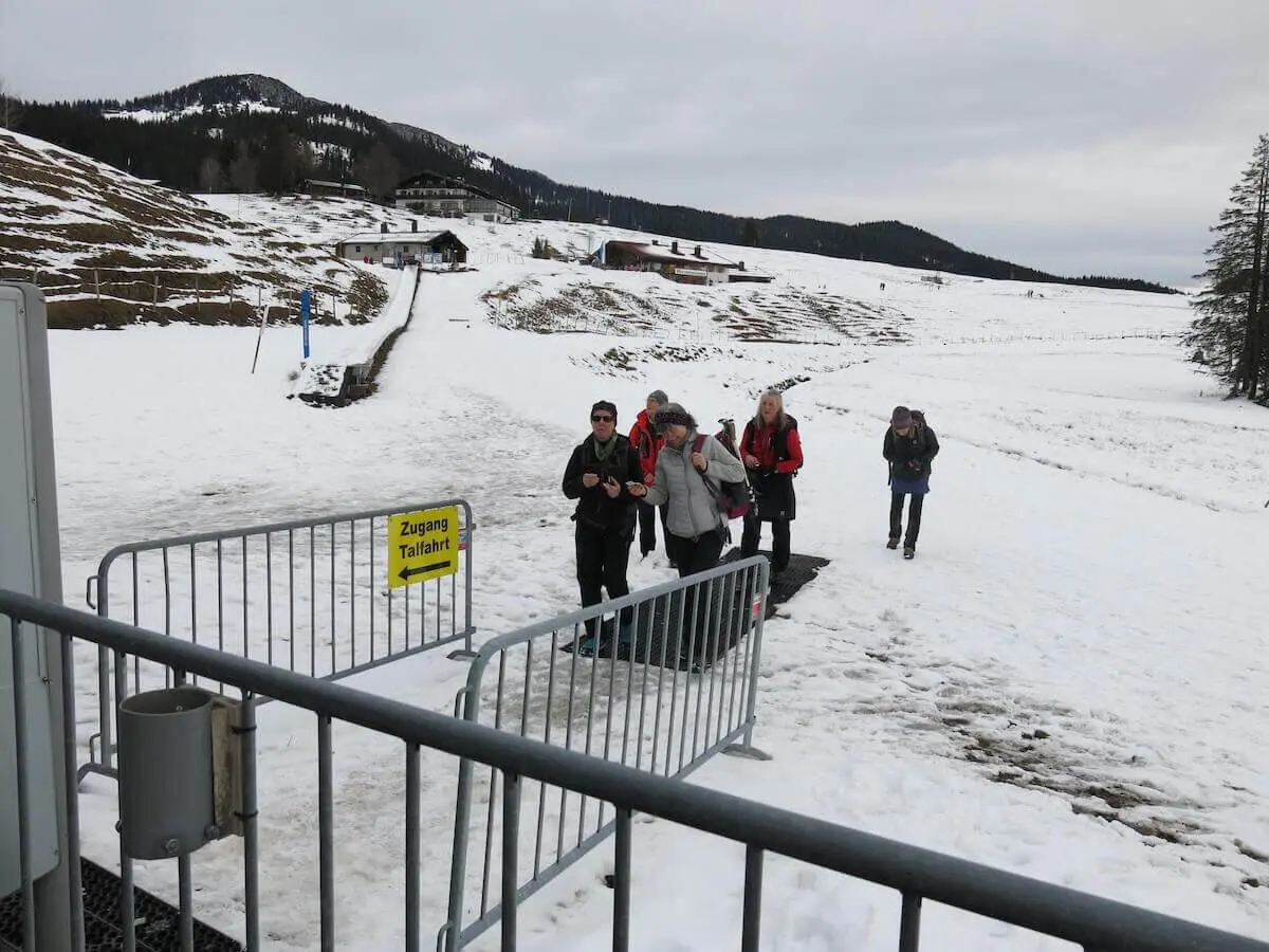Mehrere Wandernde erreichen über verschneiten Boden den Zugang zur Gondel-Talfahrt; Almhäuser stehen im Hintergrund. | © DAV Markt Schwaben / Erwin Matzinger