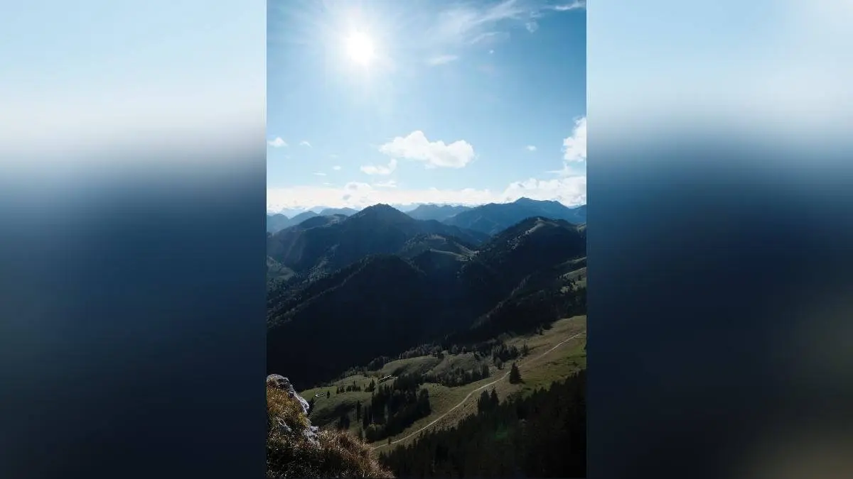 Weites Bergpanorama mit sonnigem Tal, Wiesen, Bäumen und sanften, bewaldeten Bergrücken, die in der Ferne verblassen. | © DAV Markt Schwaben/Bernhard Zech