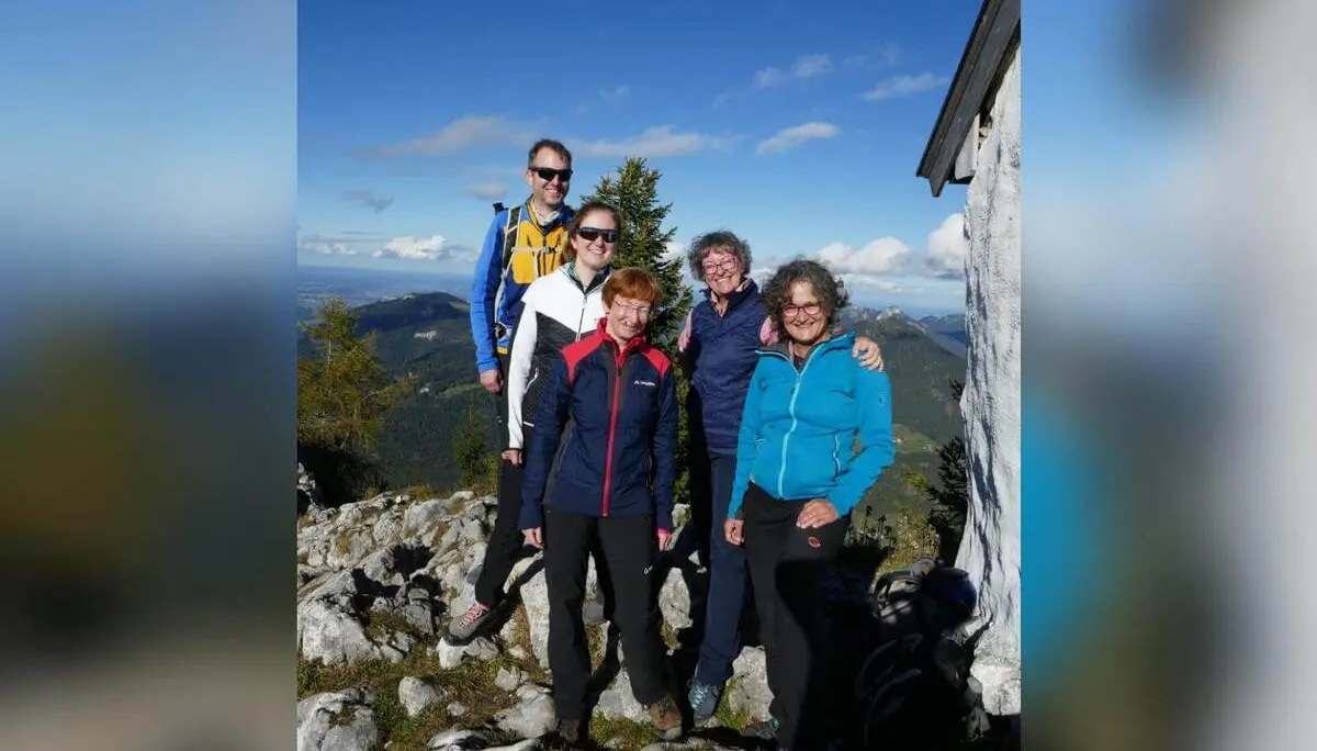Fünf Wandernde stehen auf felsigem Gipfel neben kleinem Bauwerk, dahinter weite Berglandschaft und klarer Himmel. | © DAV Markt Schwaben/Elke Kressirer