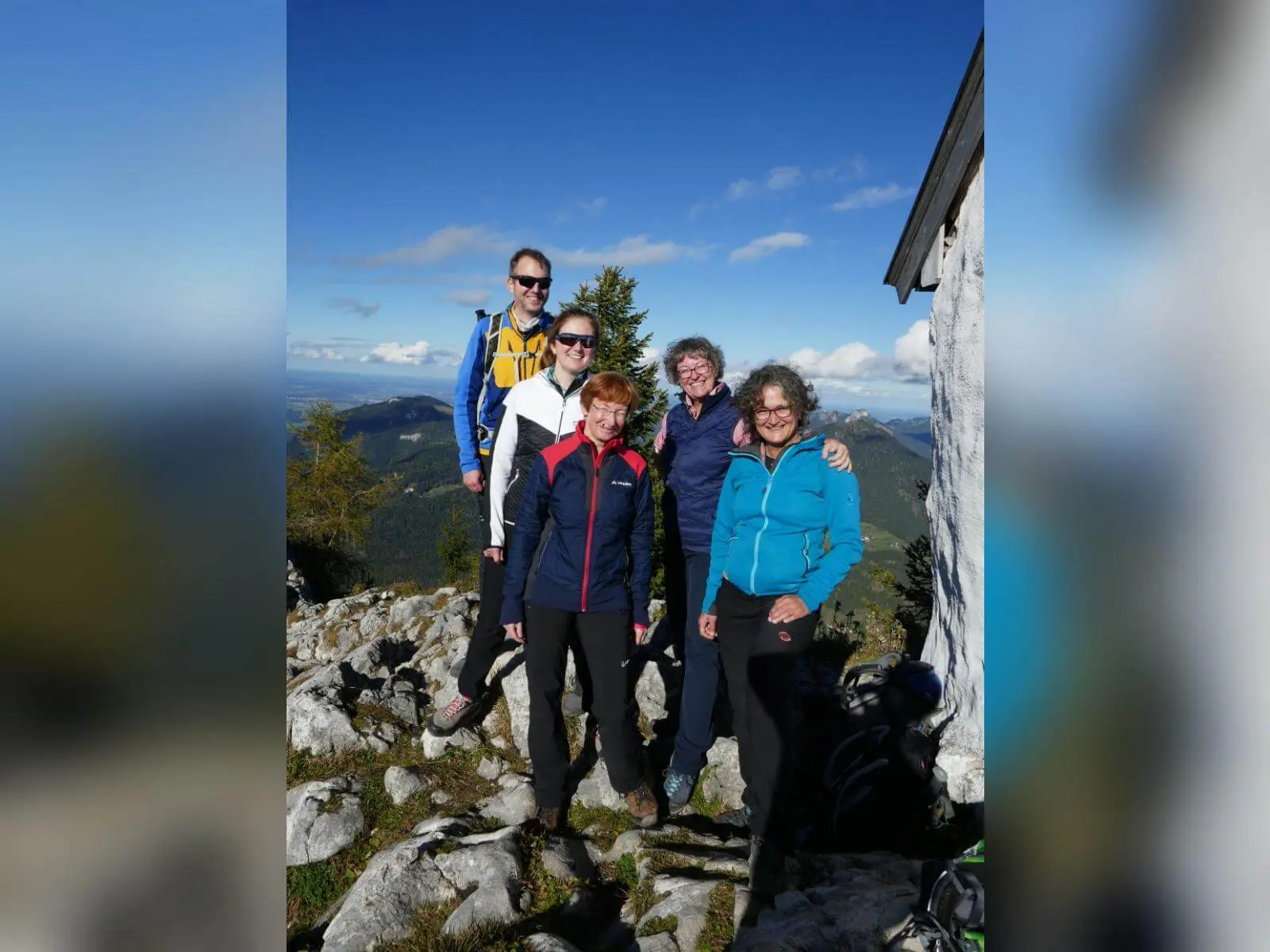Fünf Wandernde stehen auf felsigem Gipfel neben kleinem Bauwerk, dahinter weite Berglandschaft und klarer Himmel. | © DAV Markt Schwaben/Elke Kressirer
