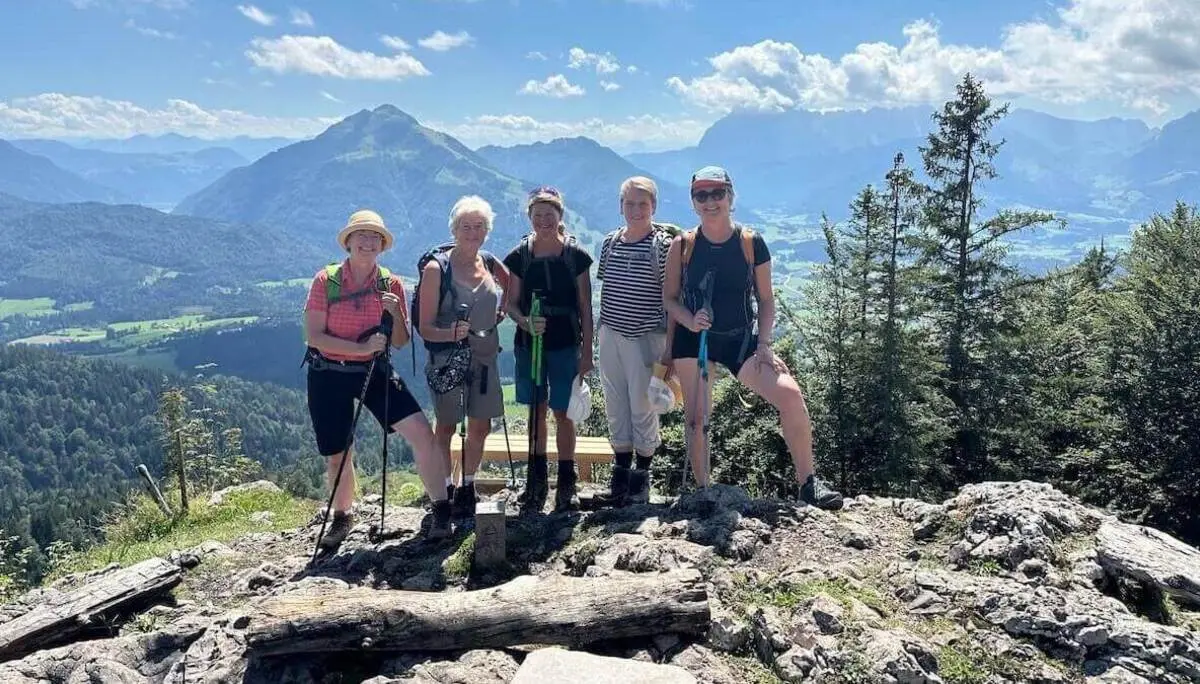Fünf Wandernde stehen auf einem felsigen Gipfel mit Stöcken und Rucksäcken; hinter ihnen weite Berglandschaft mit Wäldern, Tälern und Wolken am blauen Himmel. | © DAV Markt Schwaben/Elke Kressirer