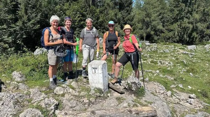Fünf Wandernde stehen um einen weißen Steinmarker auf felsigem Boden, umgeben von Gras und dichtem Wald bei Sonnenschein. | © DAV Markt Schwaben/Elke Kressirer