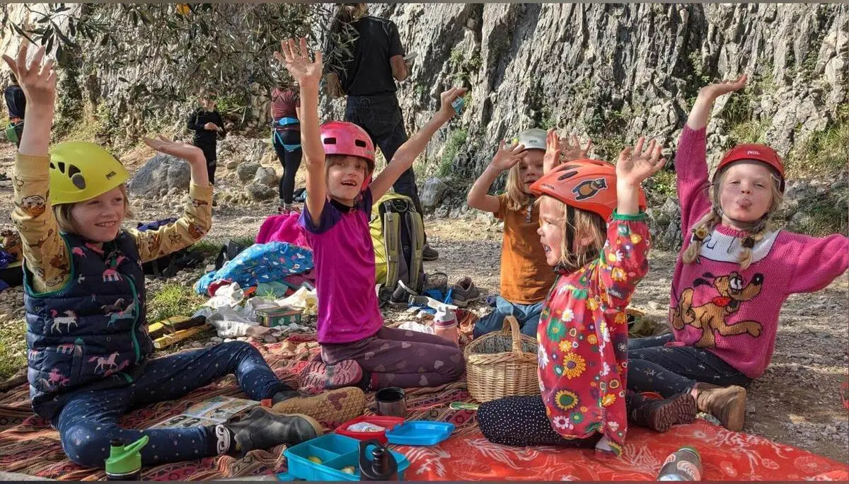 Fünf Kinder mit Kletterhelmen sitzen auf Decken vor einer Felswand in Arco und strecken bei einer Pause die Arme hoch. | © DAV Markt Schwaben / Silke Titze