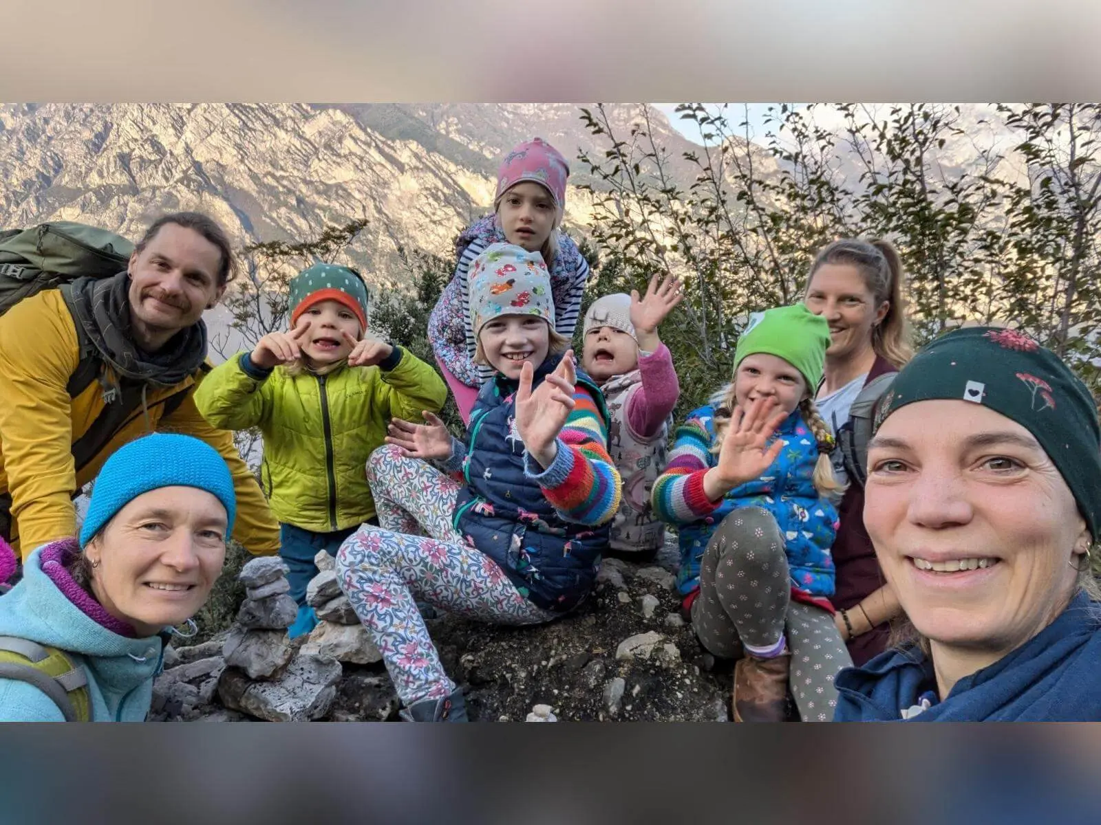 Mehrere Kinder und Erwachsene sitzen auf einem Aussichtspunkt in Arco und winken in die Kamera, dahinter ragen Felsberge auf. | © DAV Markt Schwaben / Silke Titze