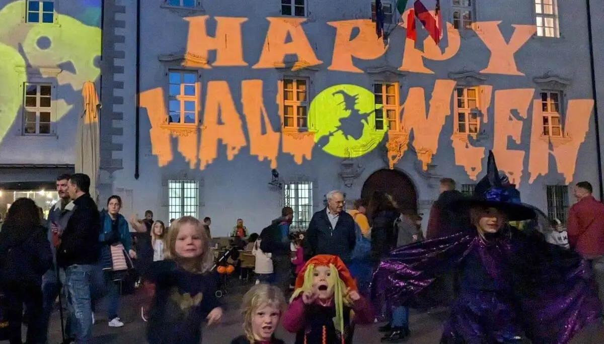 Kinder in Halloweenkostümen stehen auf einem Platz vor einem Gebäude mit großer „Happy Halloween“-Projektion und vielen Besuchern. | © DAV Markt Schwaben / Silke Titze