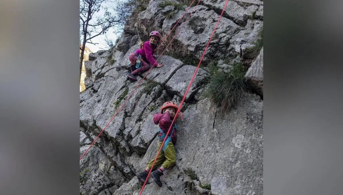 Zwei Kinder mit Helmen und Klettergurten steigen an einer gesicherten Felswand empor, rote Seile verlaufen entlang der Route. | © DAV Markt Schwaben / Silke Titze