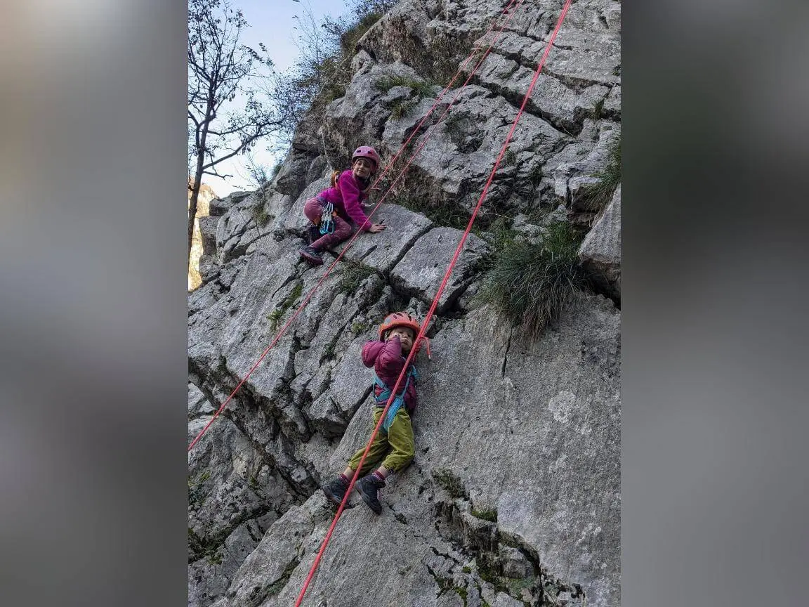 Zwei Kinder mit Helmen und Klettergurten steigen an einer gesicherten Felswand empor, rote Seile verlaufen entlang der Route. | © DAV Markt Schwaben / Silke Titze