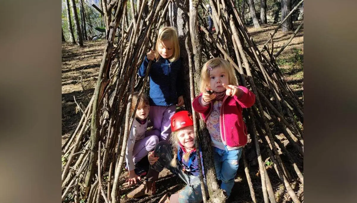 Vier Kinder sitzen und stehen in einer selbstgebauten Hütte aus Ästen im Wald bei Arco, eines trägt einen Kletterhelm. | © DAV Markt Schwaben / Silke Titze