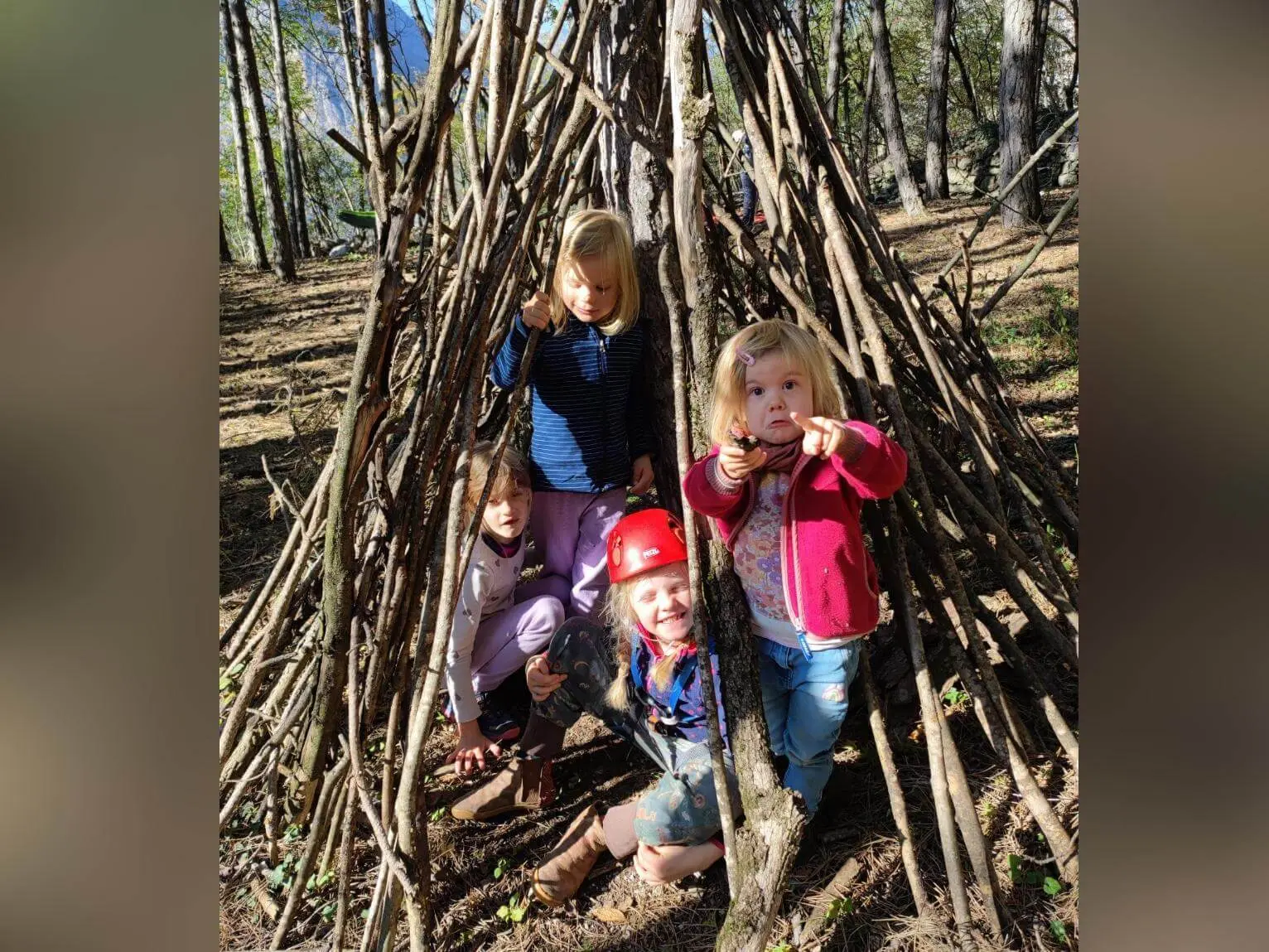 Vier Kinder sitzen und stehen in einer selbstgebauten Hütte aus Ästen im Wald bei Arco, eines trägt einen Kletterhelm. | © DAV Markt Schwaben / Silke Titze