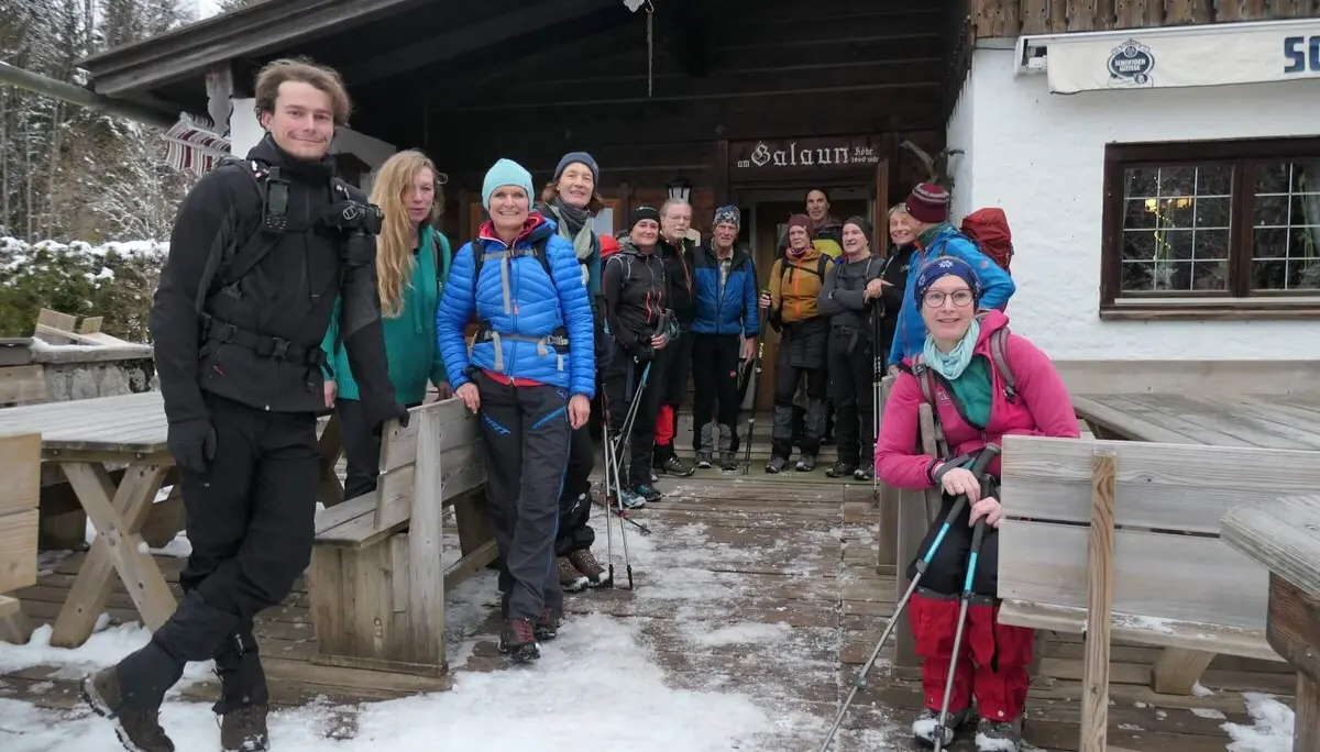 Eine Wandergruppe in Winterkleidung steht vor einer rustikalen Hütte im Schnee. Die Teilnehmenden wirken fröhlich und bereit für eine winterliche Tour. Im Hintergrund sind schneebedeckte Bäume zu sehen. | © DAV Markt Schwaben/Alfred Quiel