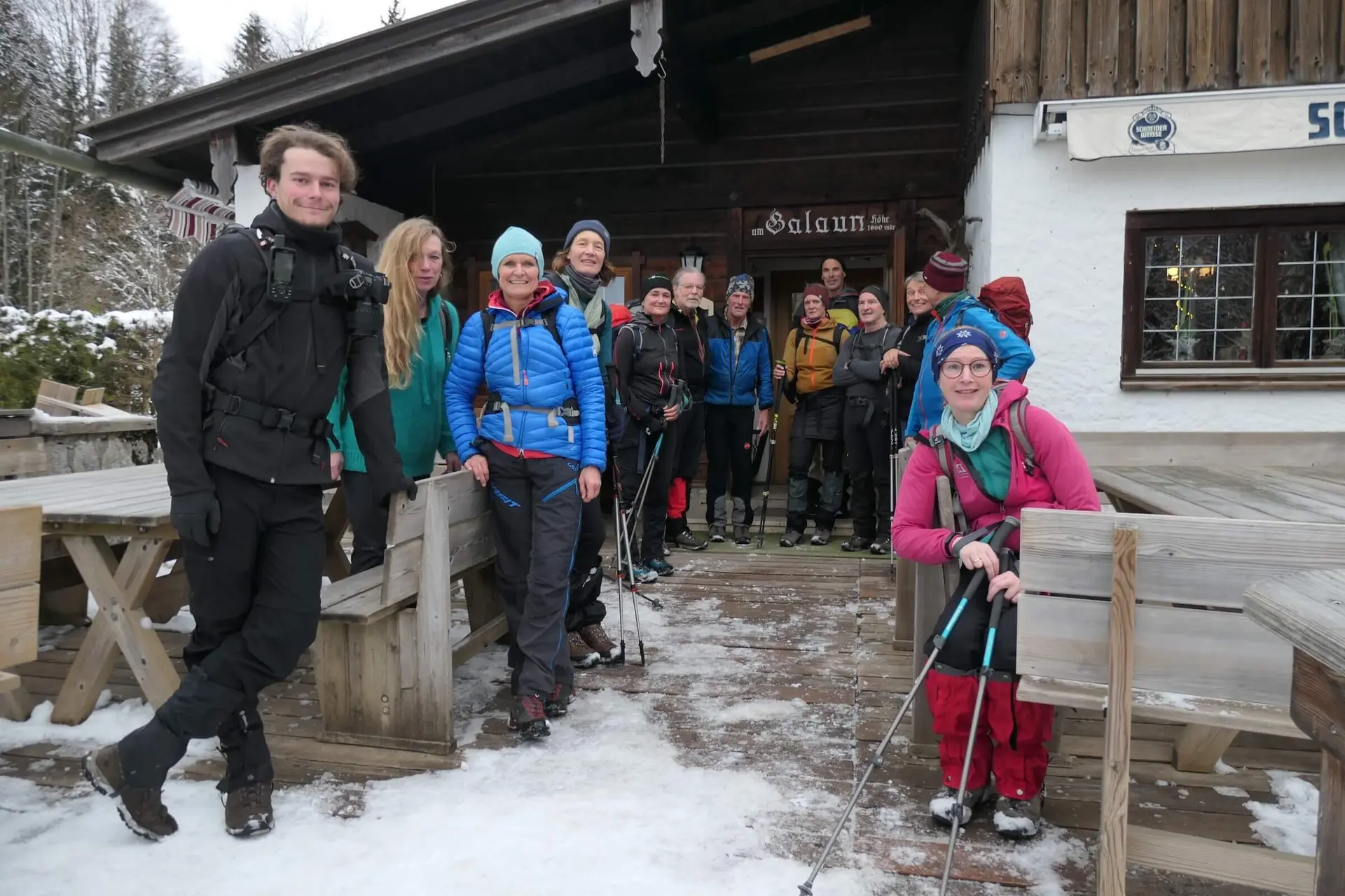 Eine Wandergruppe in Winterkleidung steht vor einer rustikalen Hütte im Schnee. Die Teilnehmenden wirken fröhlich und bereit für eine winterliche Tour. Im Hintergrund sind schneebedeckte Bäume zu sehen. | © DAV Markt Schwaben/Alfred Quiel