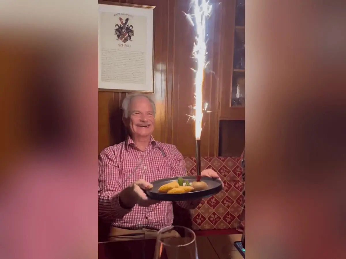 Lutz sitzt abends in holzgetäfelter Stube und hält ein Dessert mit Wunderkerze; festliche Stimmung und warmes Licht. | © DAV Markt Schwaben · Foto: Edith Zerrle