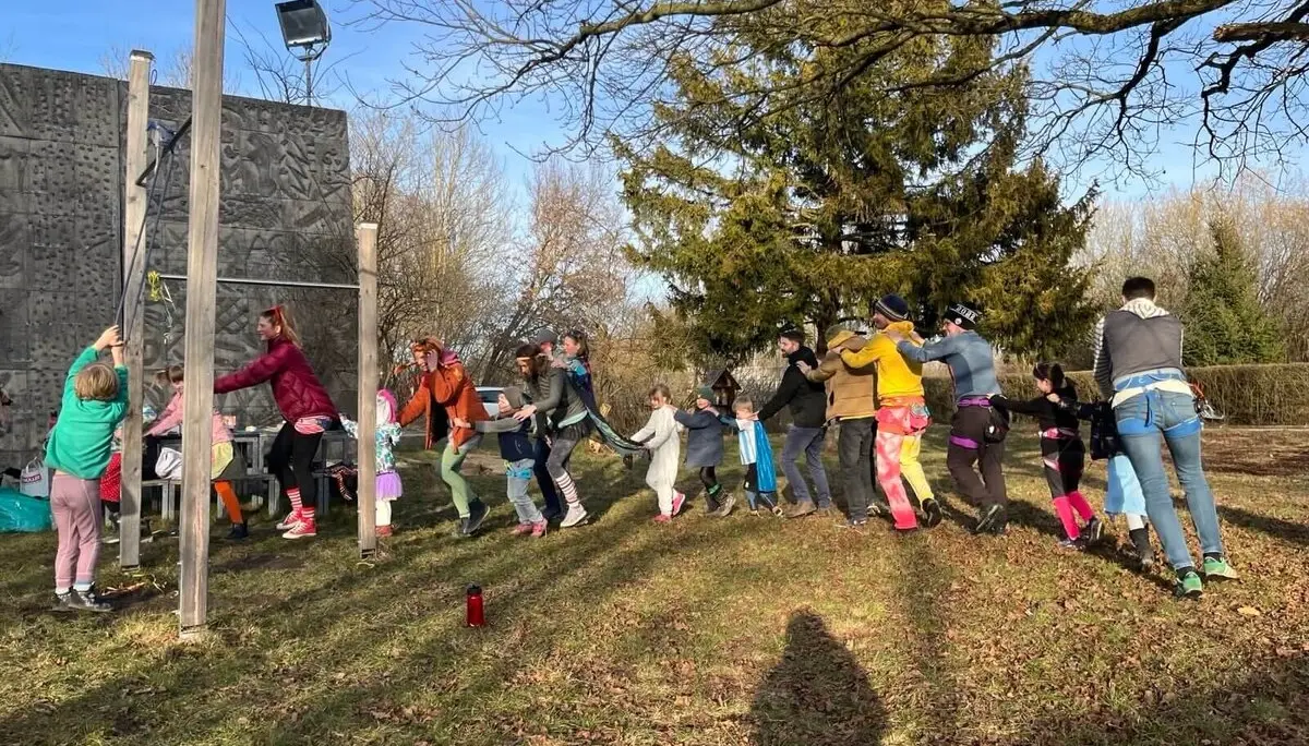 Eine Gruppe von Erwachsenen und Kindern in farbenfrohen und verspielten Outfits draußen auf einer Wiese, lächelnd und mit Spaß bei einer Polonaise. | © DAV Markt Schwaben