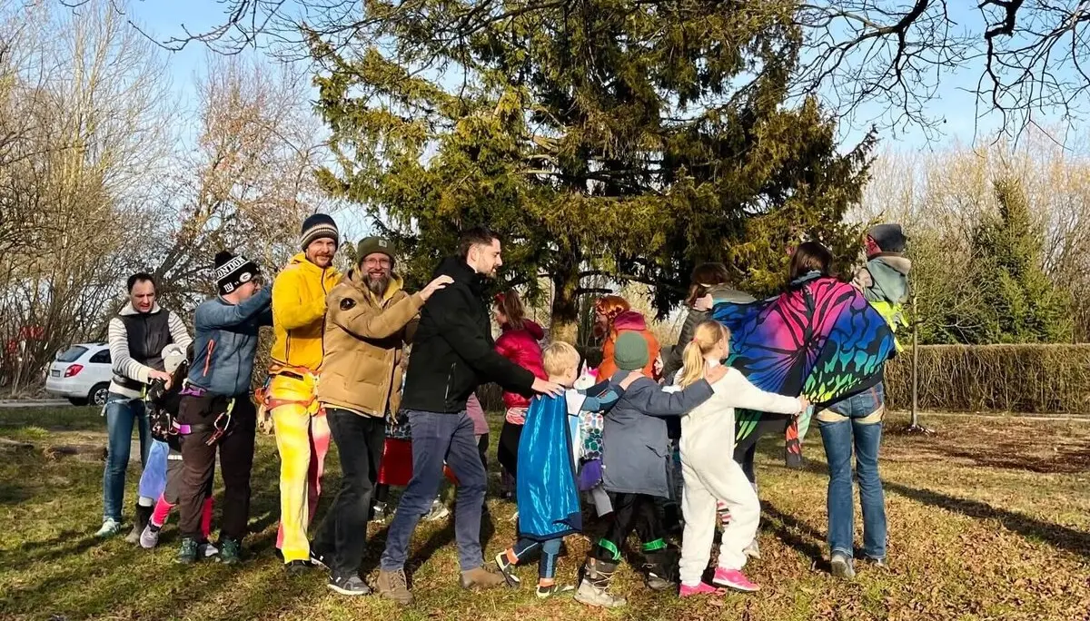 Eine Gruppe von Erwachsenen und Kindern in farbenfrohen und verspielten Outfits draußen auf einer Wiese, lächelnd und mit Spaß bei einer Polonaise. | © DAV Markt Schwaben