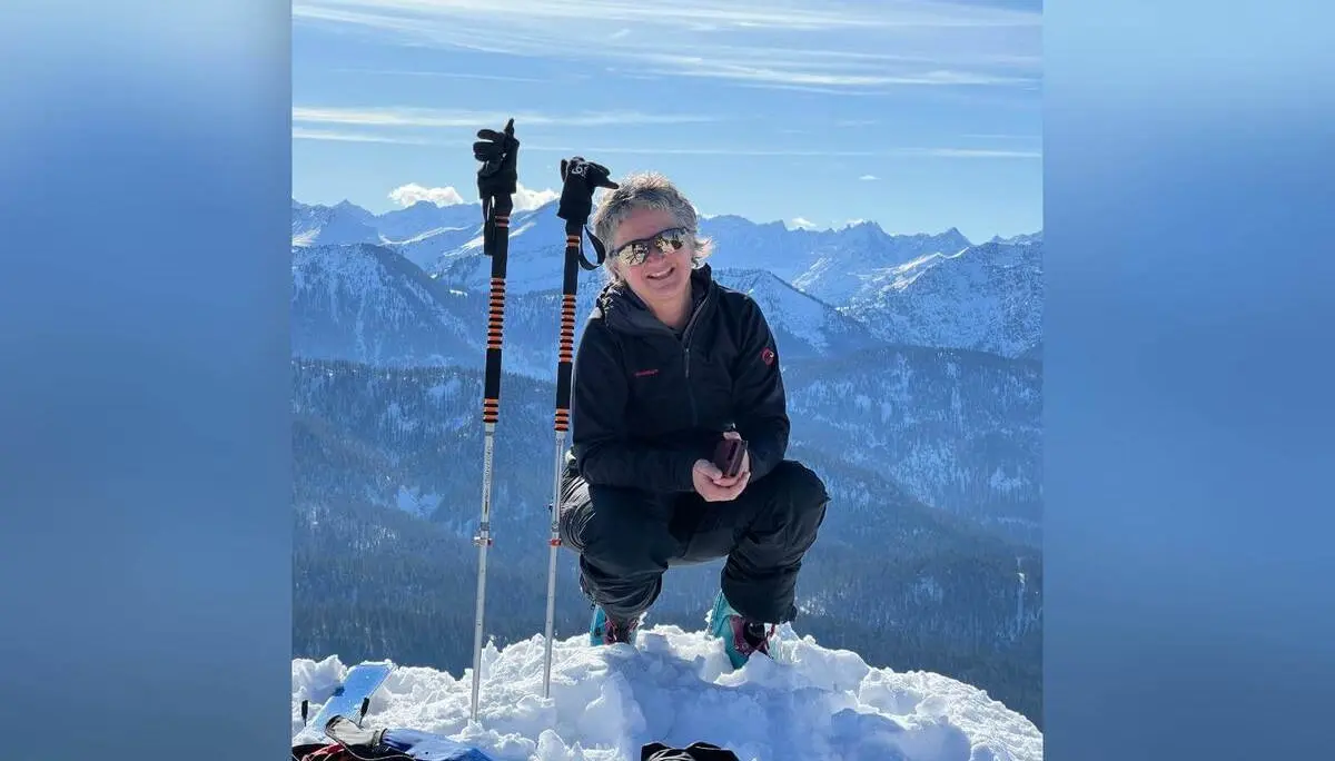 Person kniet im Schnee auf einem Gipfel neben Skistöcken, im Hintergrund erstreckt sich ein weites, sonniges Bergpanorama.Provide your feedback on BizChat | © DAV Markt Schwaben/Elke Kressirer
