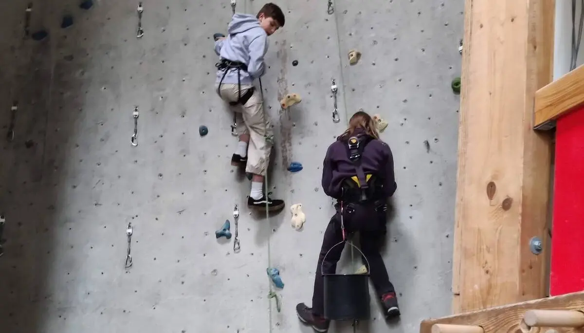 Zwei Personen arbeiten an einer Kletterwand mit bunten Griffen, tragen Sicherheitsgurte und Kletterausrüstung. | © DAV Markt Schwaben