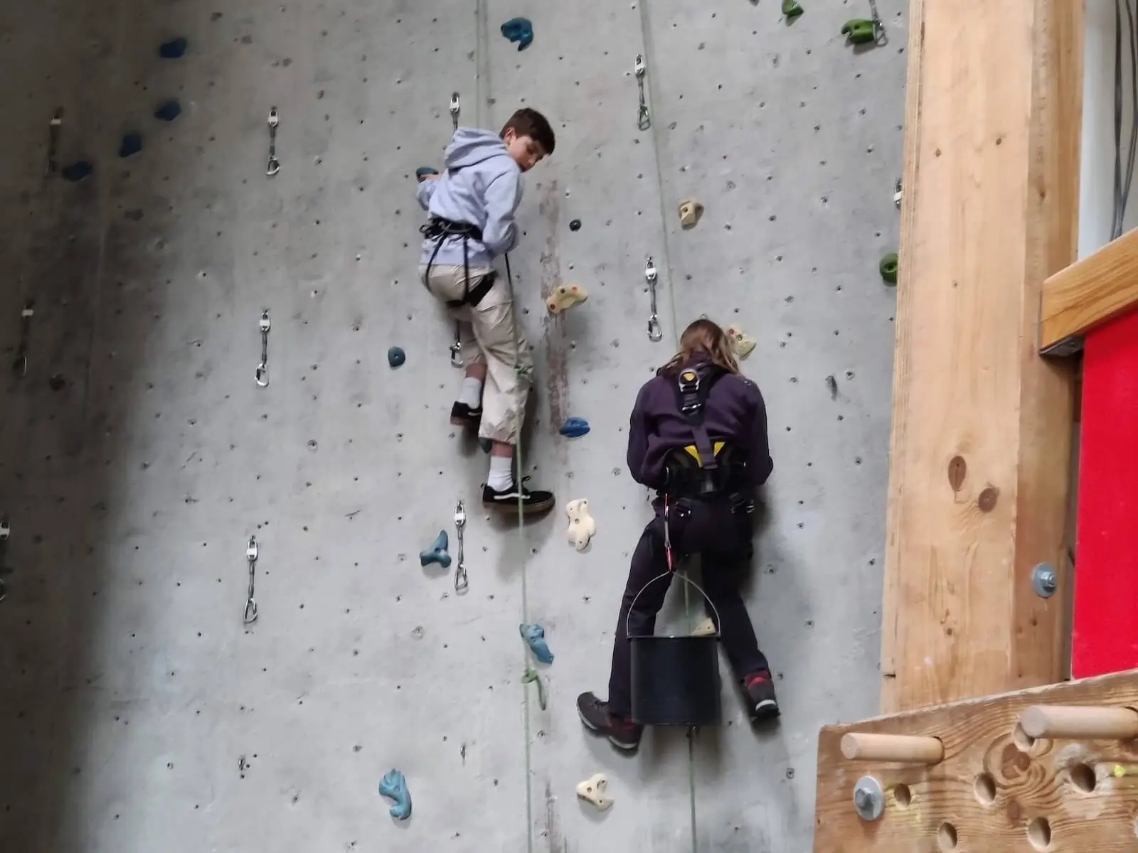 Zwei Personen arbeiten an einer Kletterwand mit bunten Griffen, tragen Sicherheitsgurte und Kletterausrüstung. | © DAV Markt Schwaben