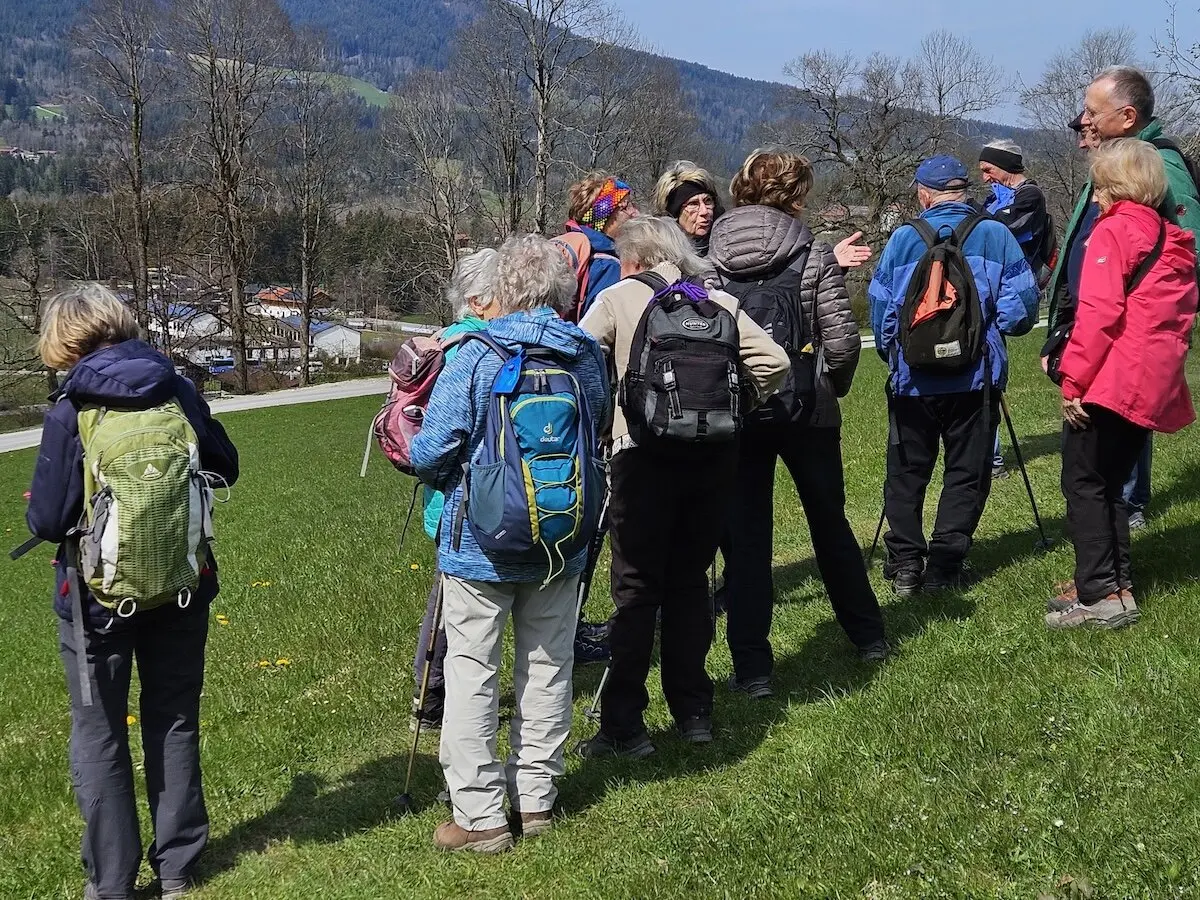 Wandergruppe mit Rucksäcken und Wanderstöcken steht auf einer Wiese mit Blick auf ein idyllisches Tal, umgeben von Bäumen und Hügeln. Ein schöner Moment der gemeinsamen Naturerkundung. | © DAV Markt Schwaben | Foto Hubert Inhofer