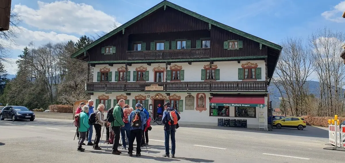 Wandergruppe steht vor einem traditionellen Gasthaus mit grünen Fensterläden und dekorierter Fassade, bereit für eine Tour in die umliegenden Berge. | © DAV Markt Schwaben | Foto Hubert Inhofer