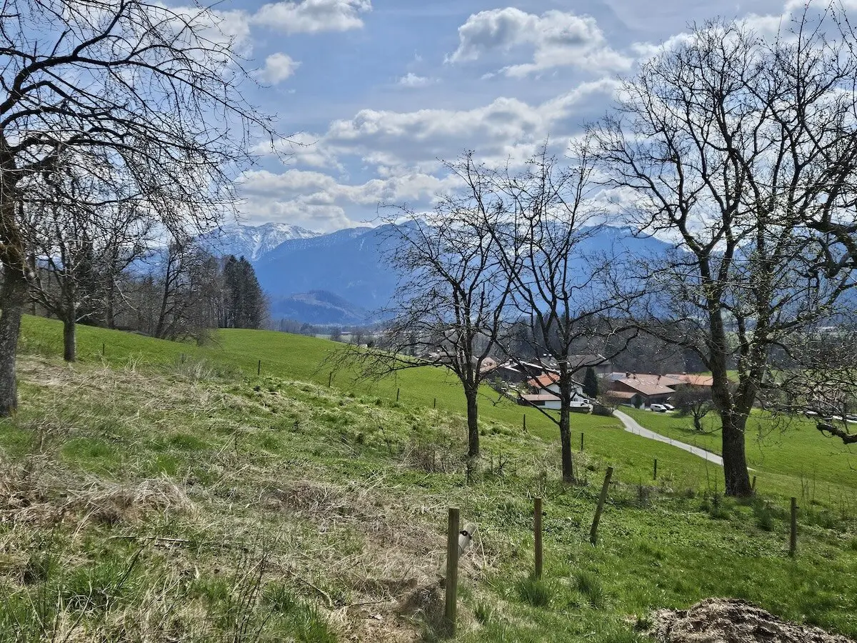 Dorf mit roten Dächern und gewundenem Weg, eingebettet in grüne Felder und Bäume, mit schneebedeckten Bergen im Hintergrund. | © DAV Markt Schwaben | Foto Hubert Inhofer