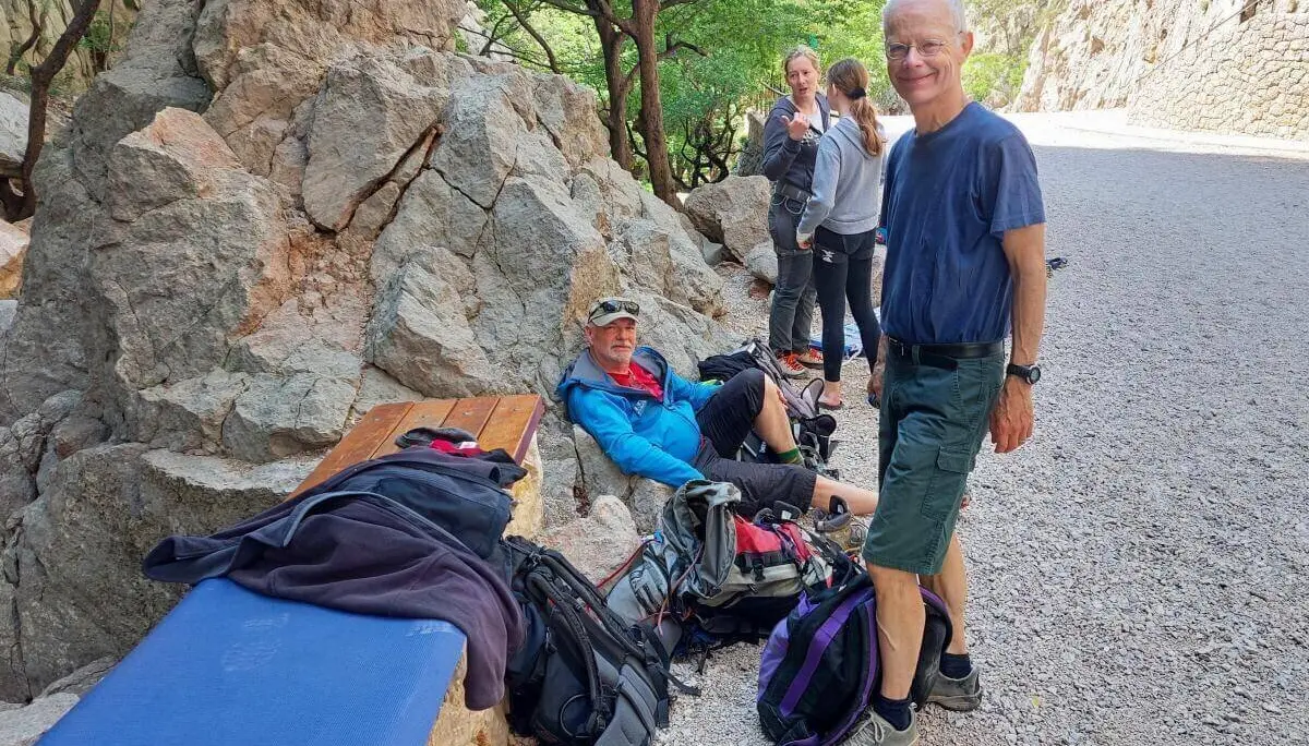 Fünf Personen ruhen an einem schattigen Platz mit Felsen und Bäumen; Rucksäcke und Ausrüstung liegen bereit. | © DAV Markt Schwaben | Foto Lutz Gründel