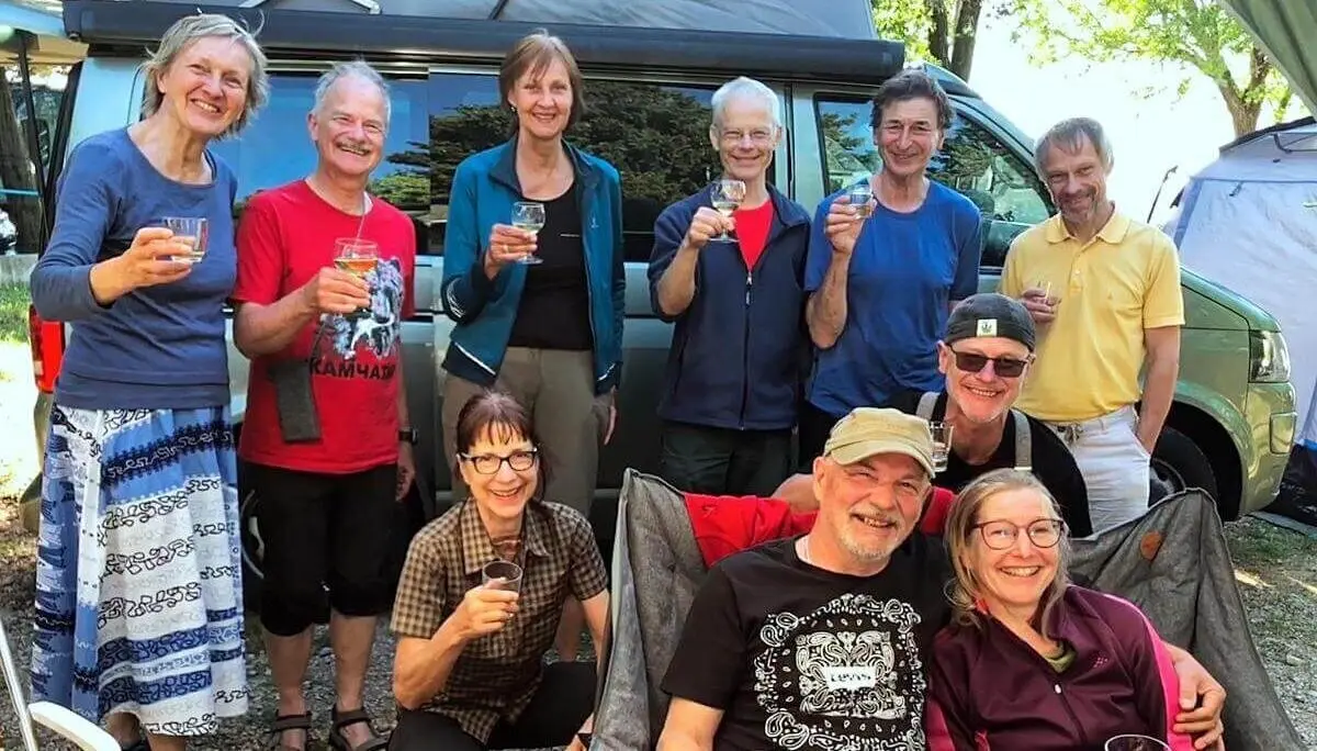Zehn Erwachsene feiern vor Campervan; zwei sitzen vorn, andere stehen lachend im Hintergrund. | © DAV Markt Schwaben | Foto Hildegard Petschik