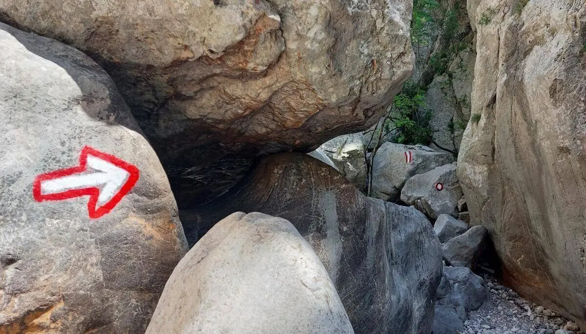 Rote Markierungen auf Felsen weisen durch schmale Passage; grobes Gelände mit wenig Vegetation. | © DAV Markt Schwaben | Foto Lutz Gründel