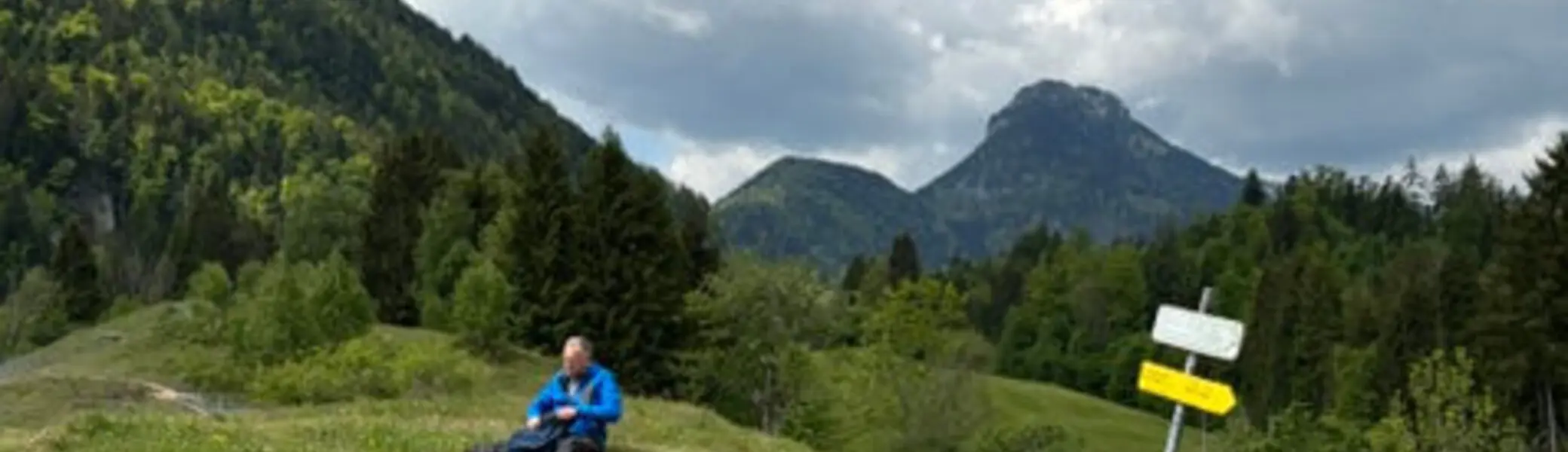 Seniorengruppe auf Wanderung bei Oberaudorf – Pause auf einer Holzbank mit Bergblick unter wolkigem Himmel. | © DAV Markt Schwaben / Hubert Inhofer