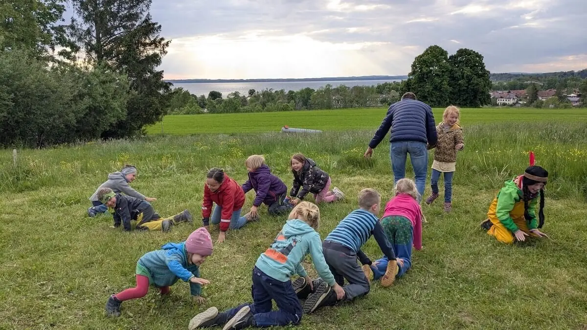 Eine Gruppe von Kindern spielt fröhlich mit einem Erwachsenen auf einer grünen Wiese. Sie bewegen sich aktiv und genießen die gemeinsame Zeit. | © DAV Markt Schwaben | Foto: Familiengruppe