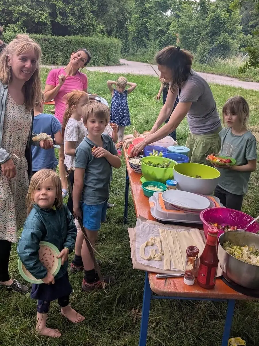 Kinder und Erwachsene versammeln sich an einem gedeckten Tisch mit Salaten und Grillgut – geselliges Familienpicknick im Freien. | © DAV Markt Schwaben | Foto Silke Titze