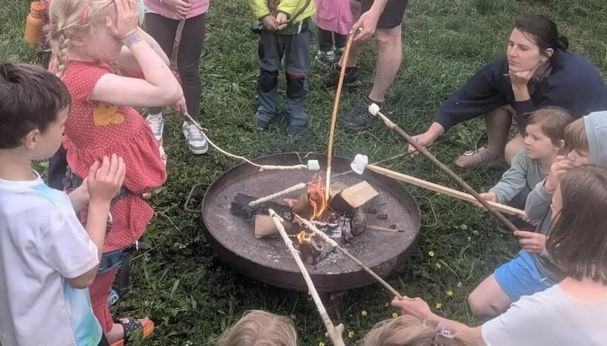 Kinder und Erwachsene sitzen rund ums Lagerfeuer und rösten Marshmallows – fröhliches Beisammensein. | © DAV Markt Schwaben | Foto Silke Titze