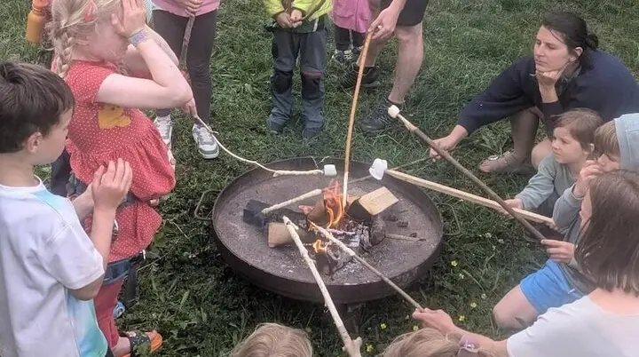 Kinder und Erwachsene sitzen rund ums Lagerfeuer und rösten Marshmallows – fröhliches Beisammensein. | © DAV Markt Schwaben | Foto Silke Titze