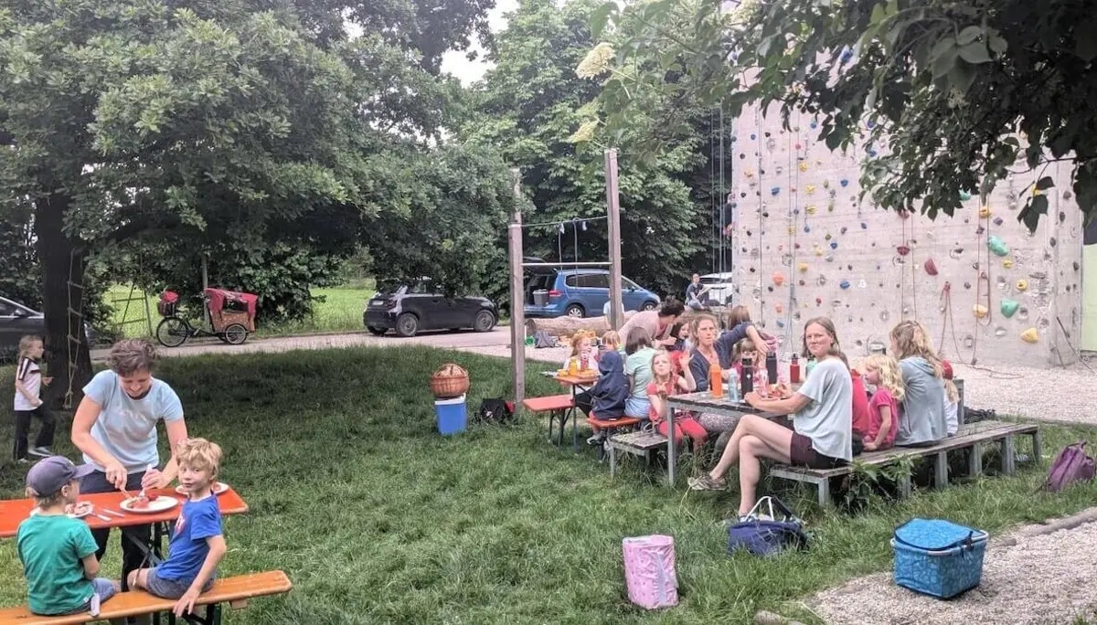 Kinder klettern an einer bunten Wand, während Familien an Tischen essen und plaudern – fröhliches Beisammensein mit Spiel und Gemeinschaft. | © DAV Markt Schwaben | Foto Silke Titze