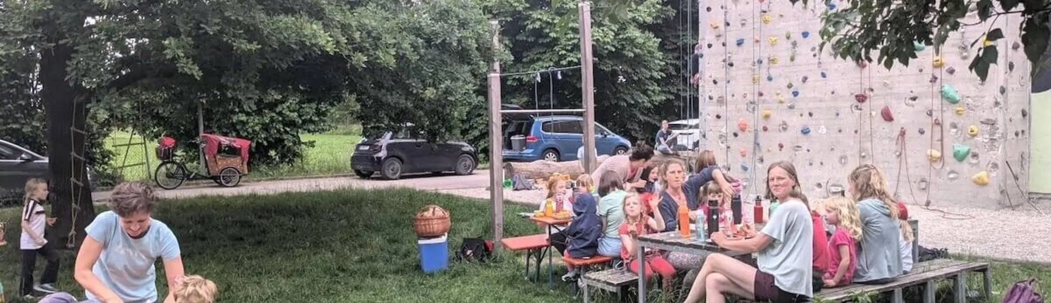 Kinder klettern an einer bunten Wand, während Familien an Tischen essen und plaudern – fröhliches Beisammensein mit Spiel und Gemeinschaft. | © DAV Markt Schwaben | Foto Silke Titze