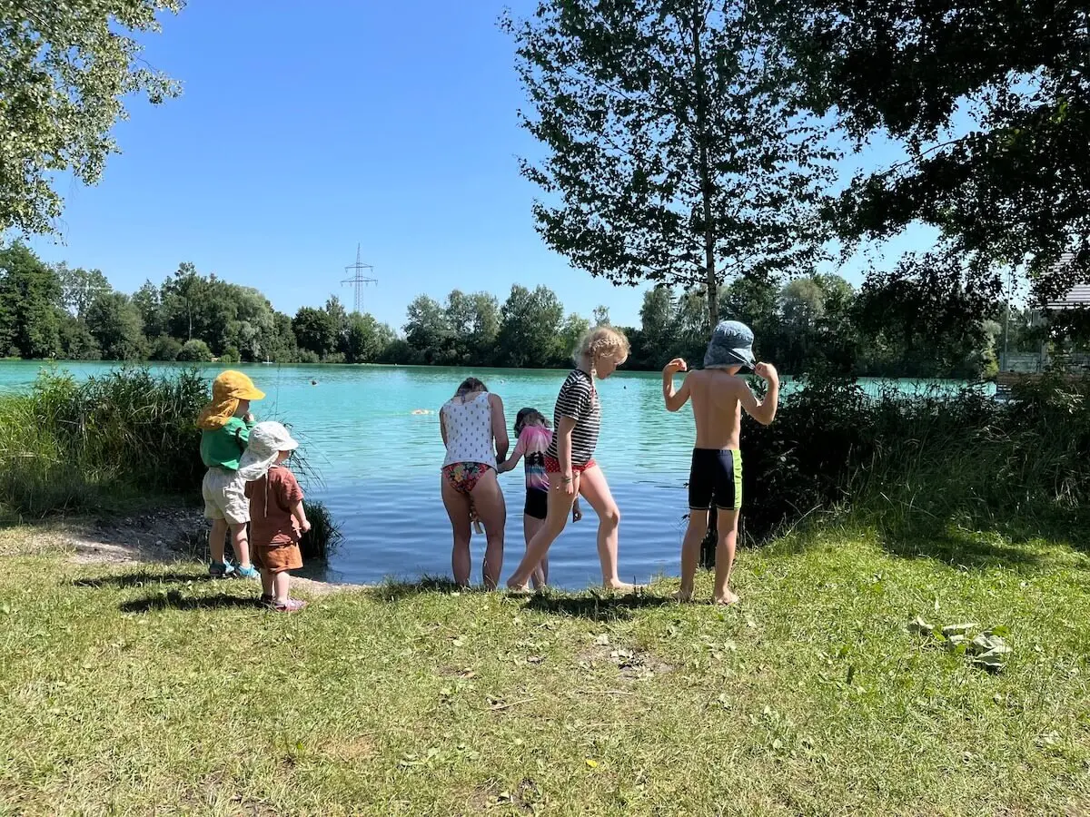 Kinder stehen am Ufer des Wiflinger Weihers, genießen die Natur nach einer gemeinsamen Radtour – ein sommerliches Familienabenteuer. | © DAV Markt Schwaben | Foto: Lara Wolff